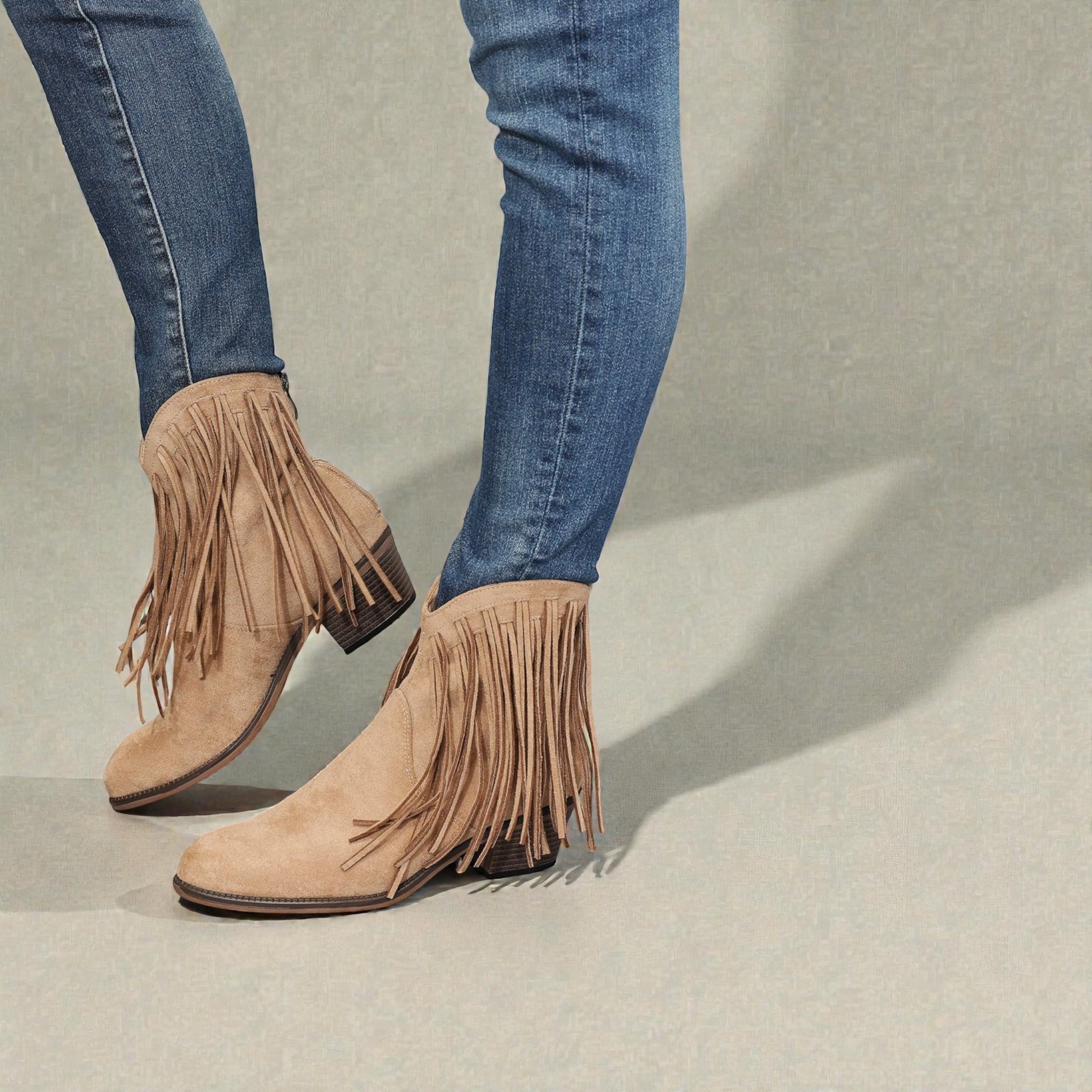 Beige fringe boots worn with blue jeans on a neutral background