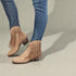 Beige fringe boots worn with blue jeans on a neutral background