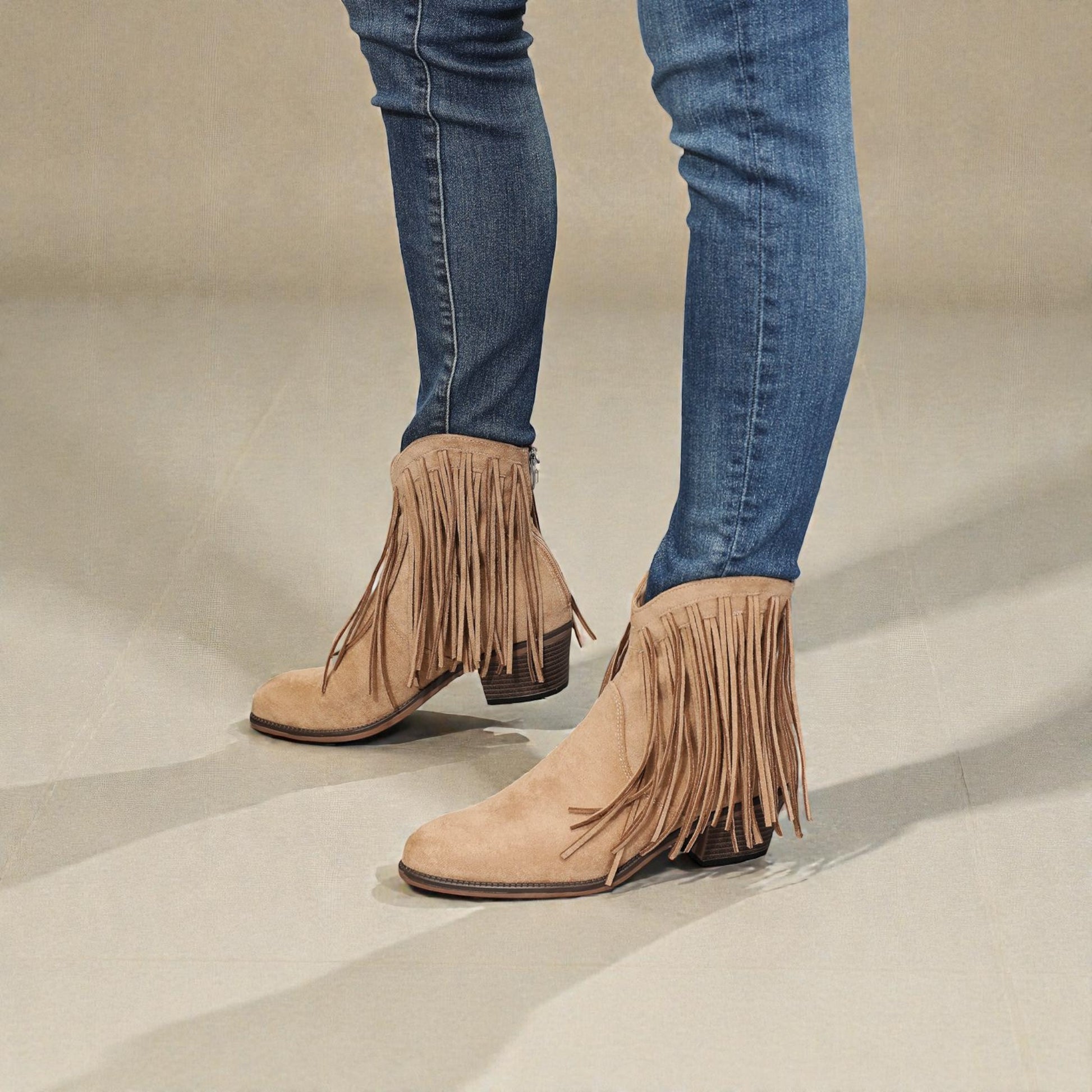 Beige fringe boots worn with blue jeans on a neutral background