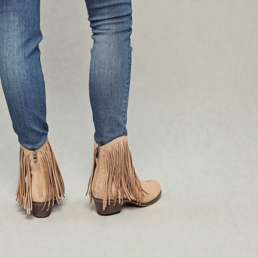 Tan fringe boots worn with blue jeans on a neutral background