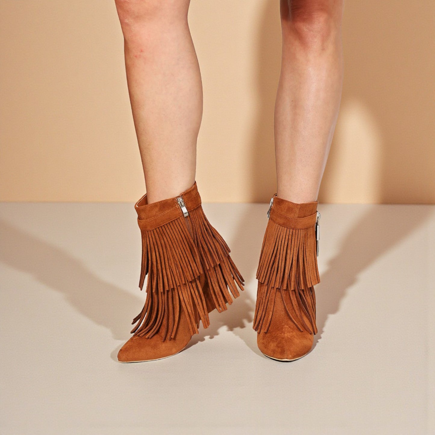 Brown suede fringe boots worn by a person on a beige background