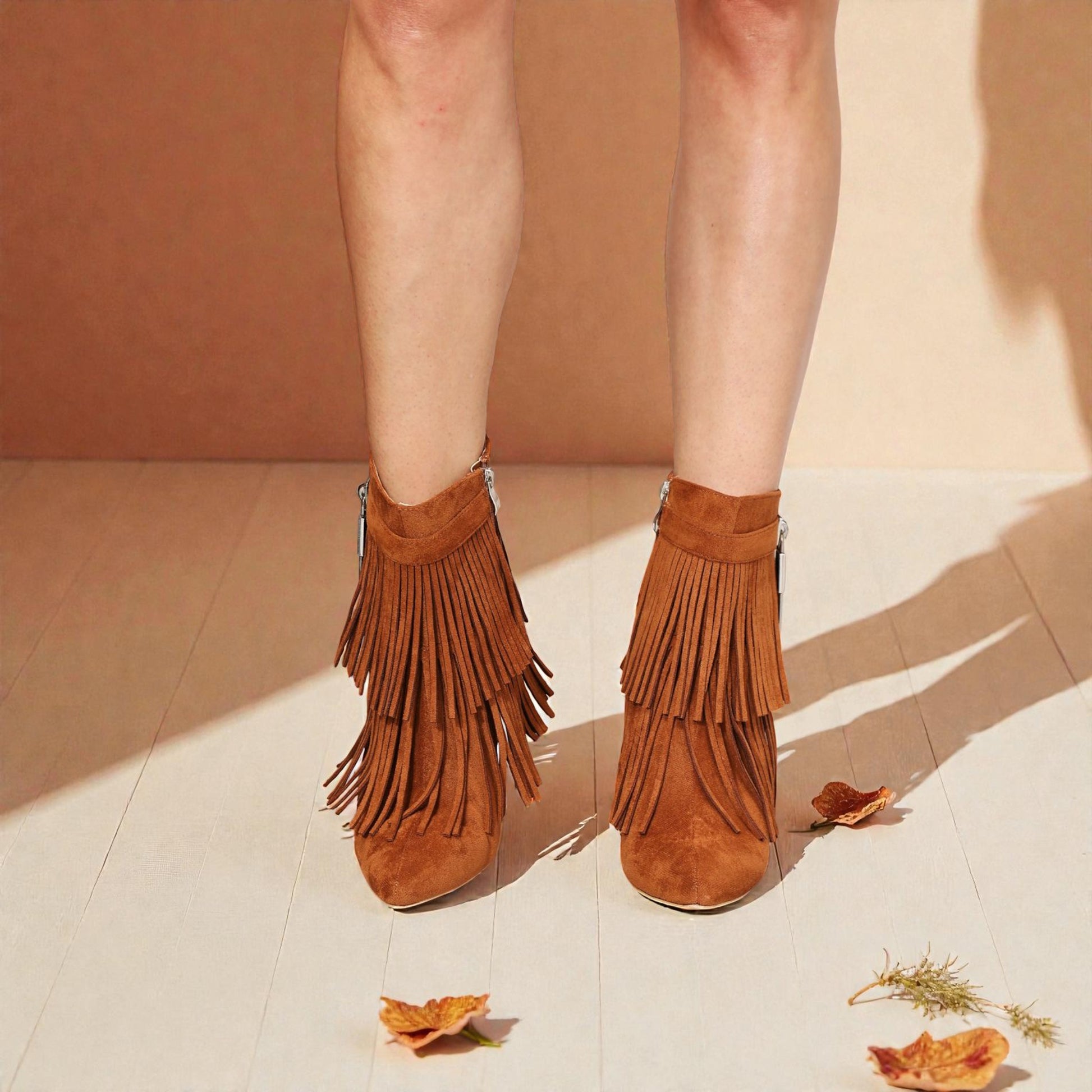 Brown suede fringe boots worn by a person on a light wooden floor.