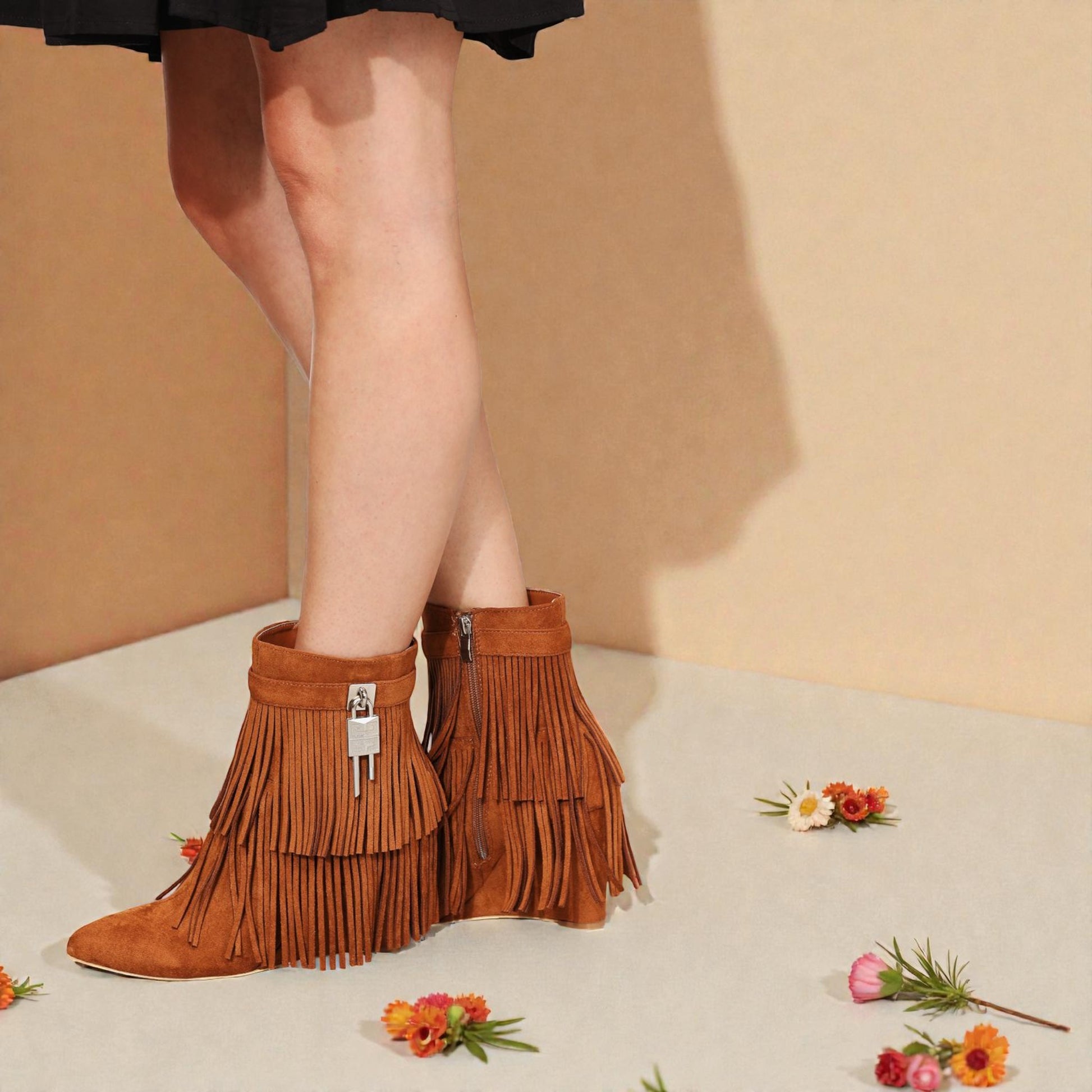 Brown fringed boots worn by a person with a beige background and flowers.
