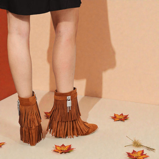 Brown fringed boots worn with a black skirt on a beige background with autumn leaves.