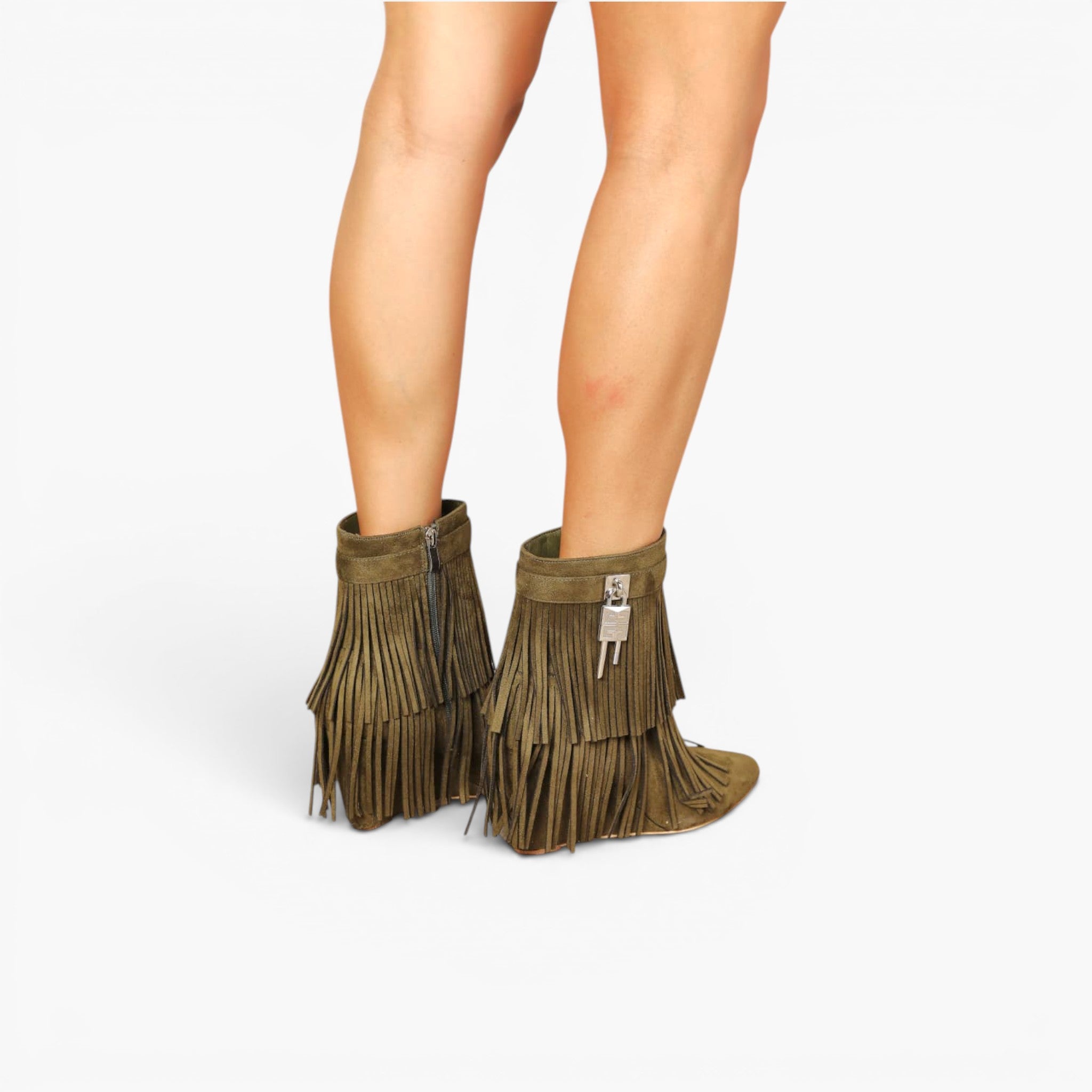 A pair of olive green fringe ankle boots with silver zipper details, shown on a model's feet against a light gray background.