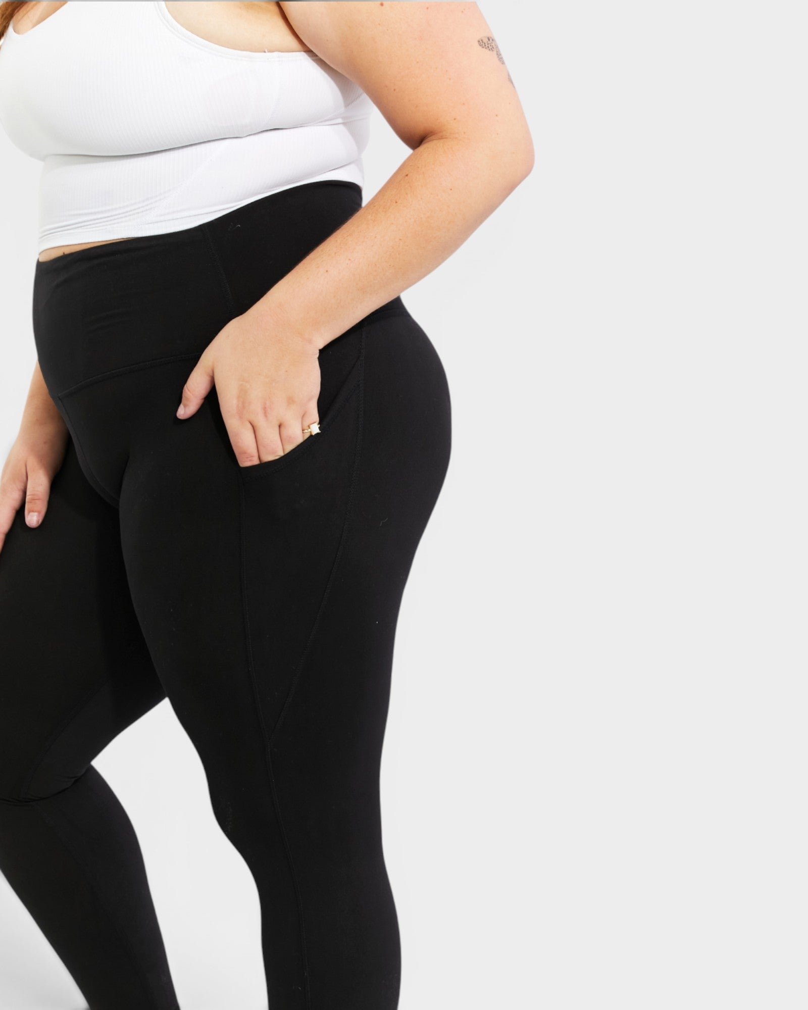 Person wearing black leggings and a white top on a light gray background