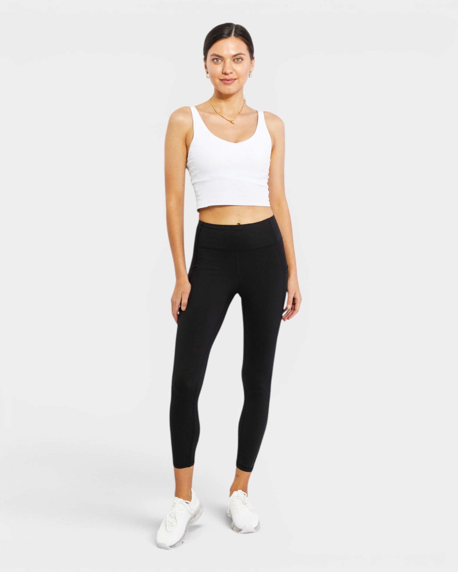 Woman wearing a white tank top and black leggings on a white background