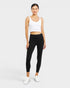 Woman wearing a white tank top and black leggings on a white background
