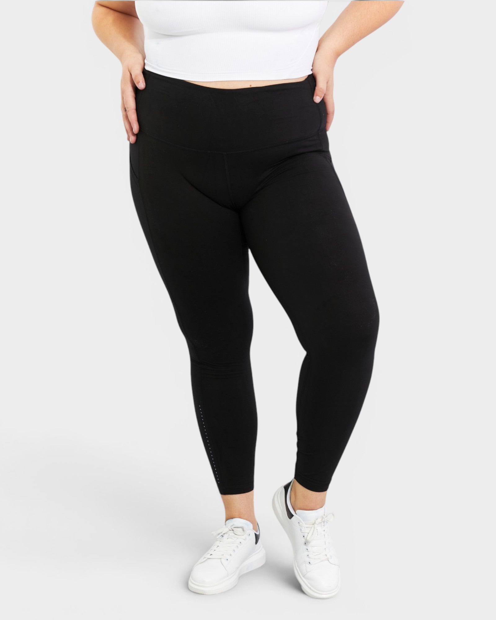 Person wearing black leggings and white sneakers on a light gray background