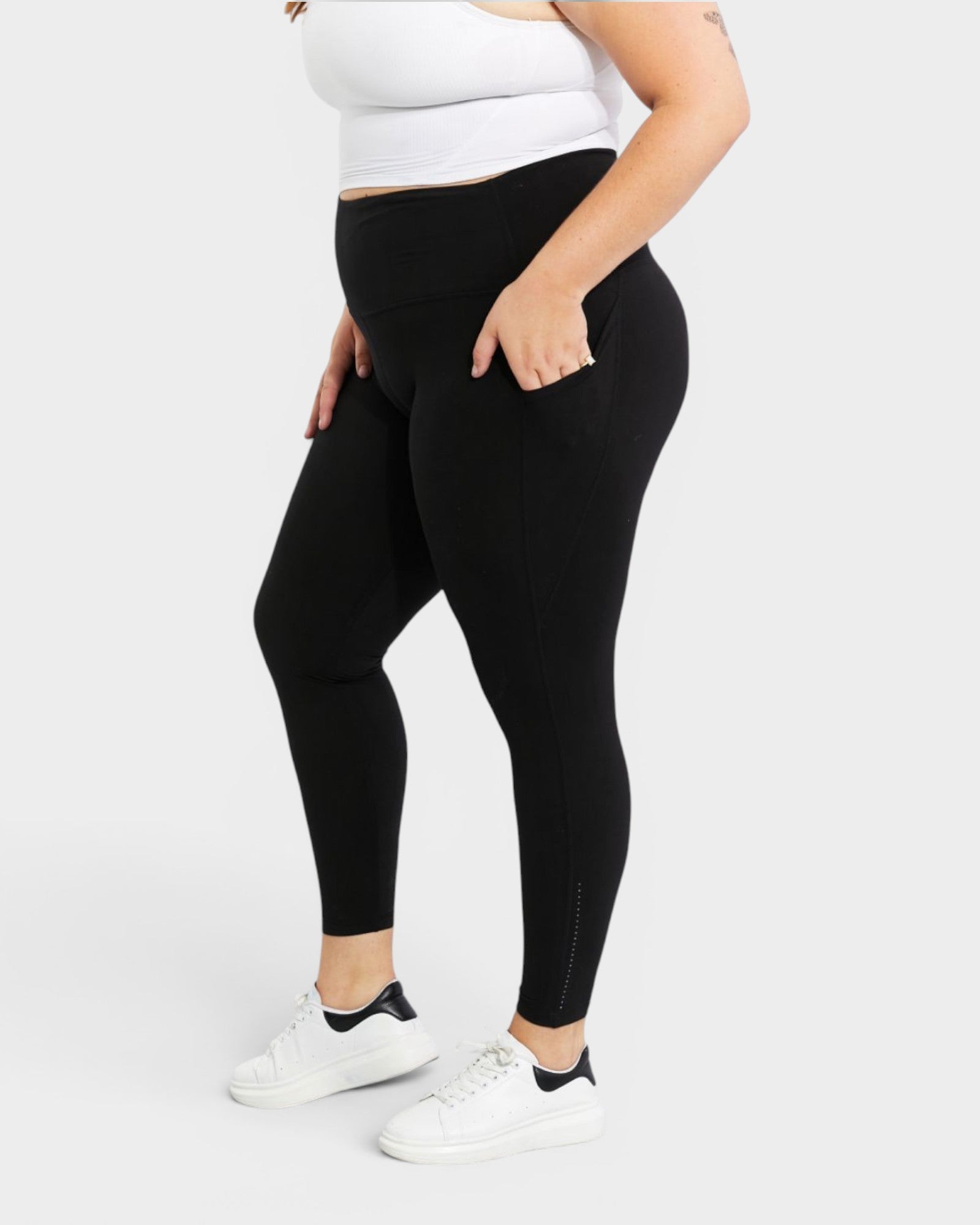 Person wearing black leggings and white sneakers on a light gray background