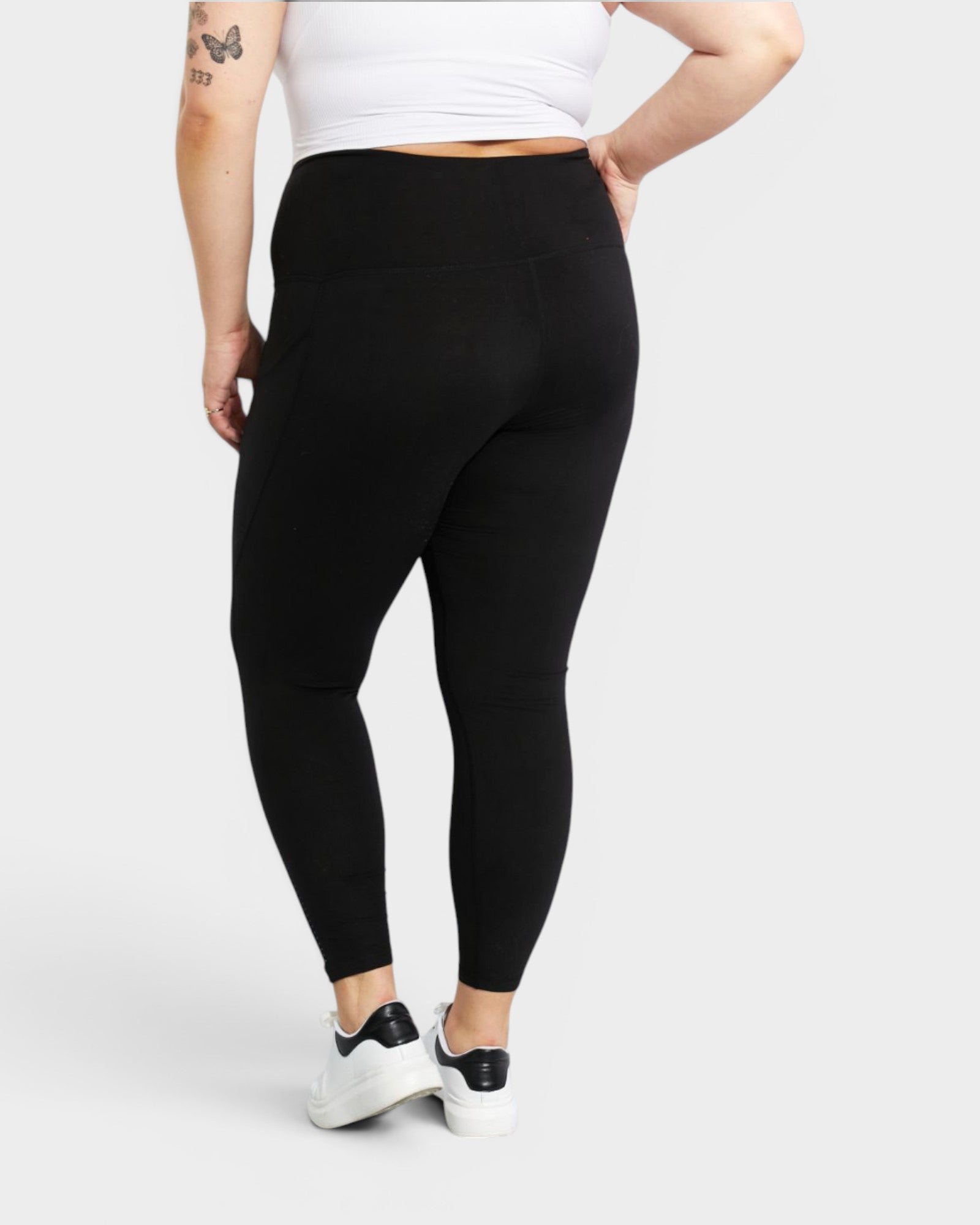 Person wearing black leggings and a white top on a light gray background