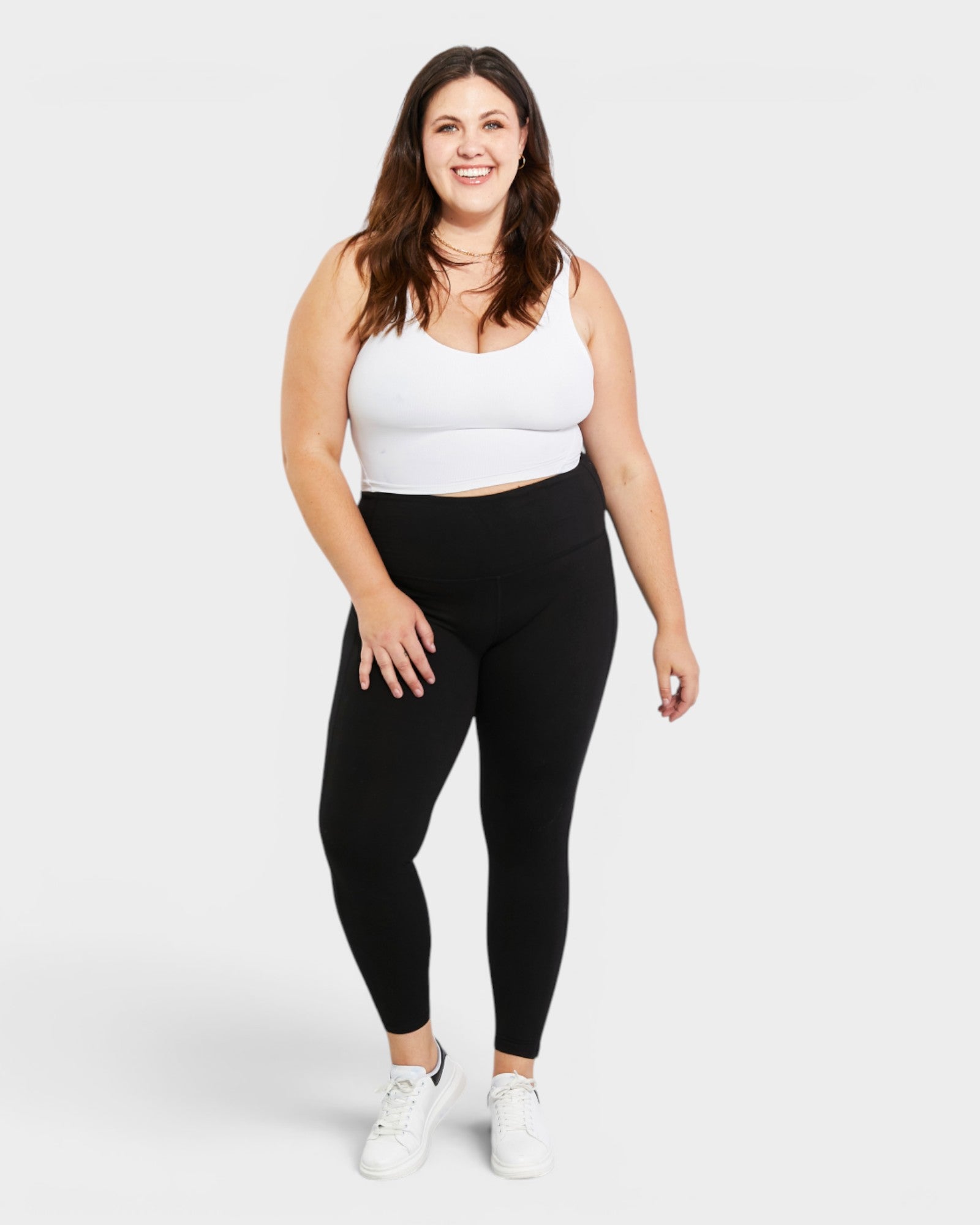 Woman wearing a white tank top and black leggings on a white background