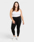 Woman wearing a white tank top and black leggings on a white background