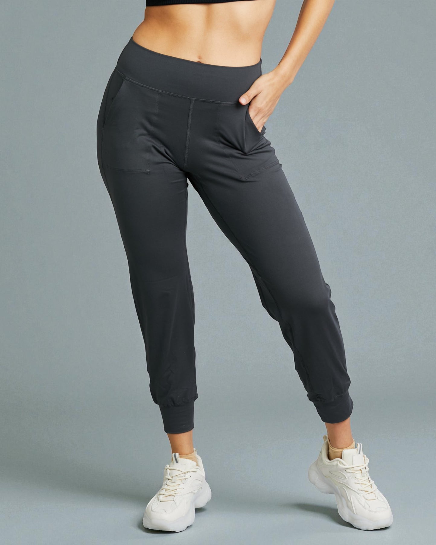 Person wearing black jogger pants and white sneakers on a gray background