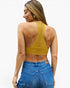 A woman shown from the back wearing a mustard yellow crochet open-back crop top and blue jeans, against a plain white studio background.