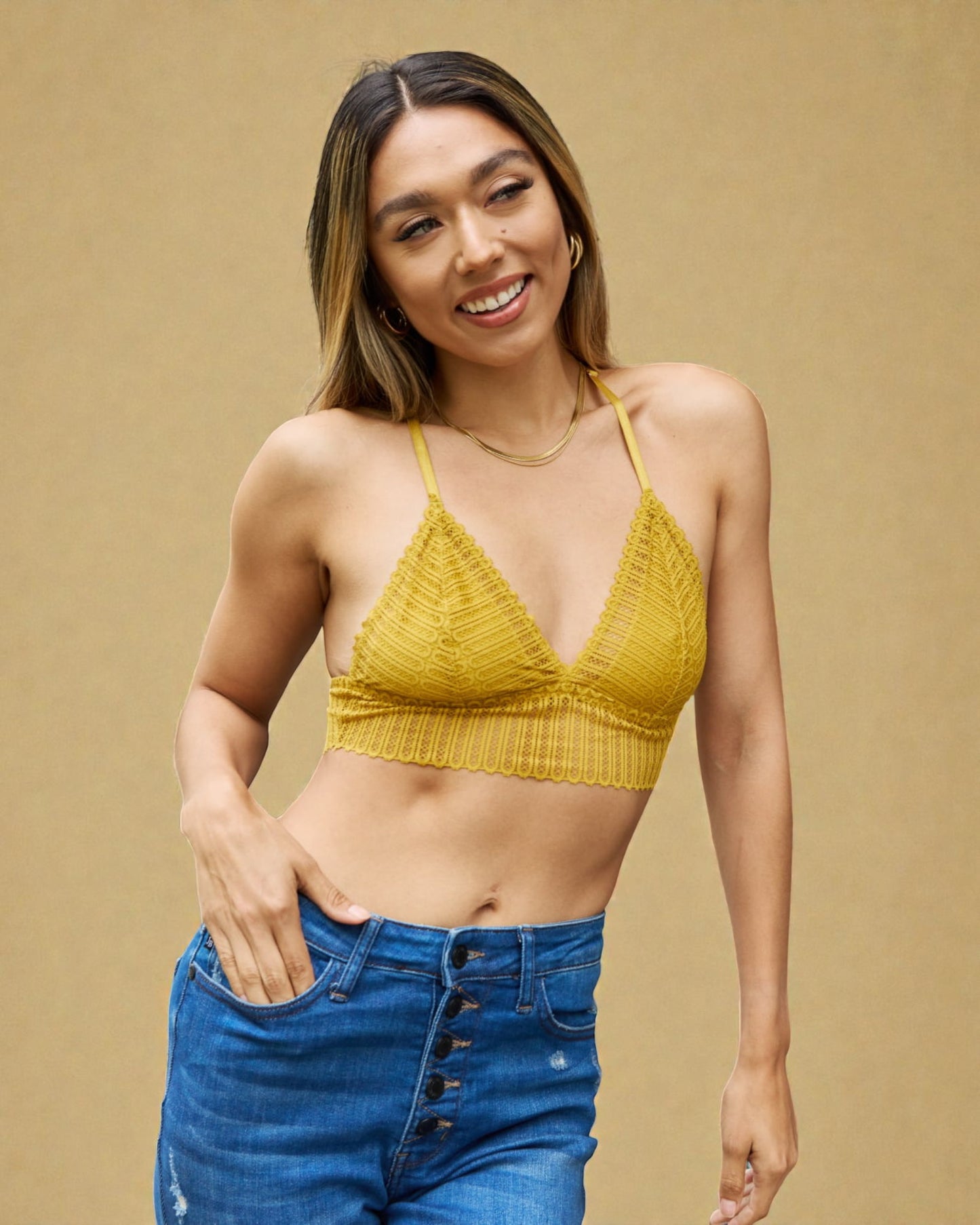 Woman wearing a yellow ribbed crop top and blue jeans on a beige background