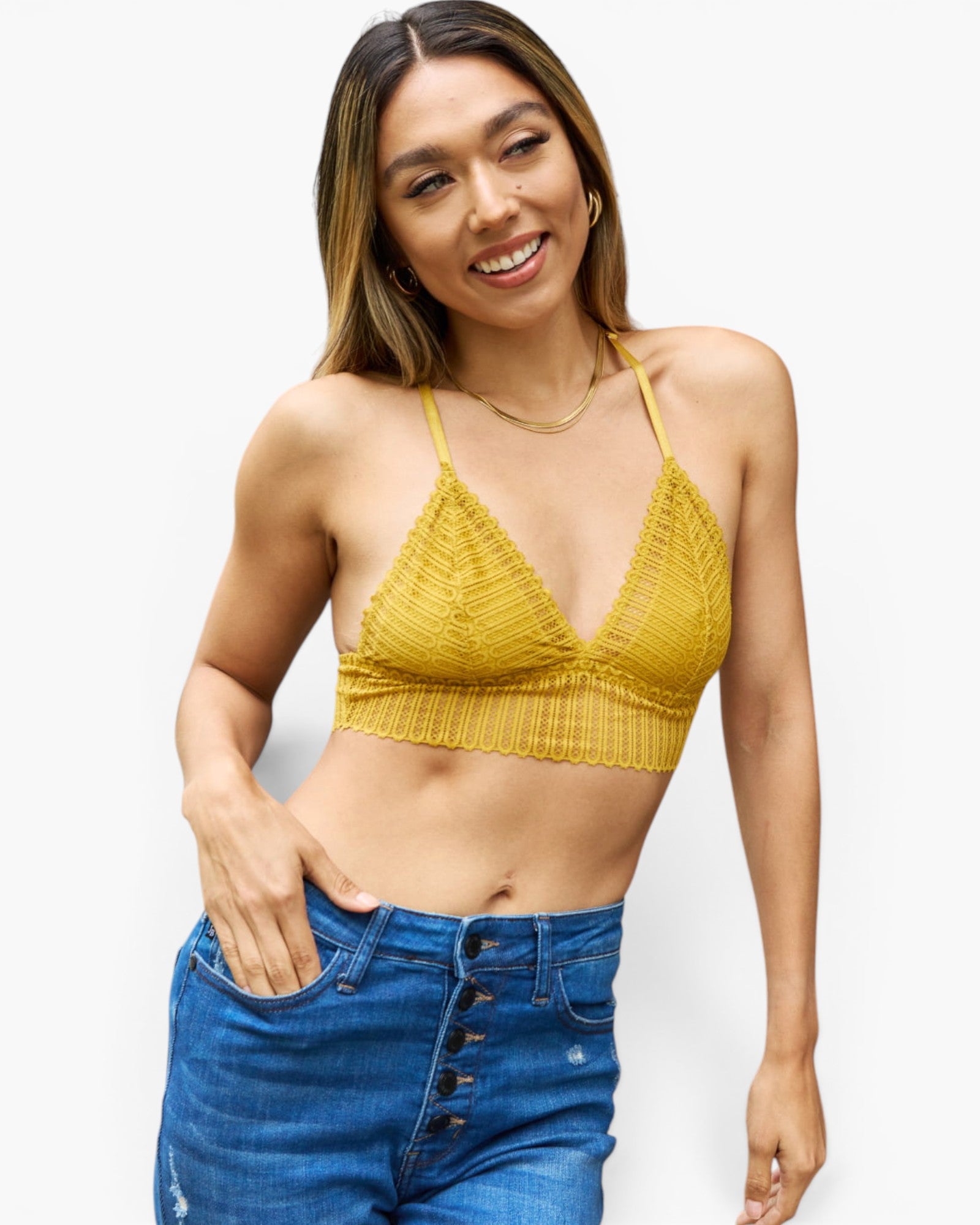 A woman modeling a textured mustard yellow knit triangle bralette top paired with high-waisted blue jeans against a plain white background.