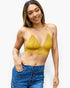 A woman modeling a textured mustard yellow knit triangle bralette top paired with high-waisted blue jeans against a plain white background.