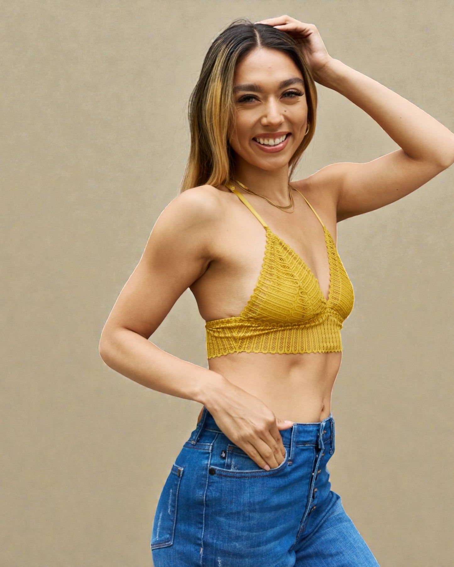 Woman wearing a yellow ribbed crop top and blue jeans against a beige background