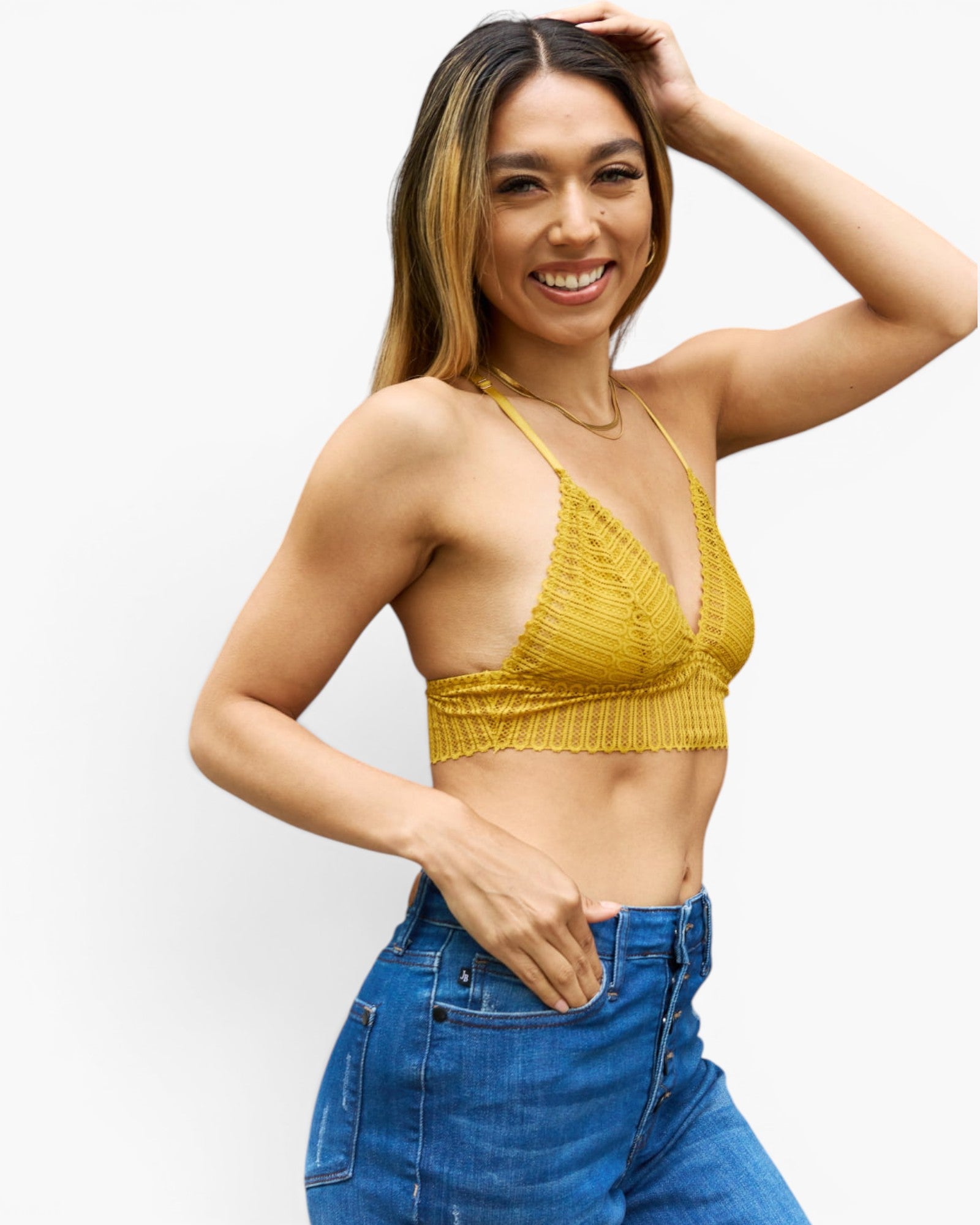 A woman modeling a yellow knit halter crop top with scalloped edges, paired with blue jeans, against a plain white background.