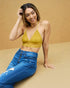 Woman wearing a yellow top and blue jeans against a beige background