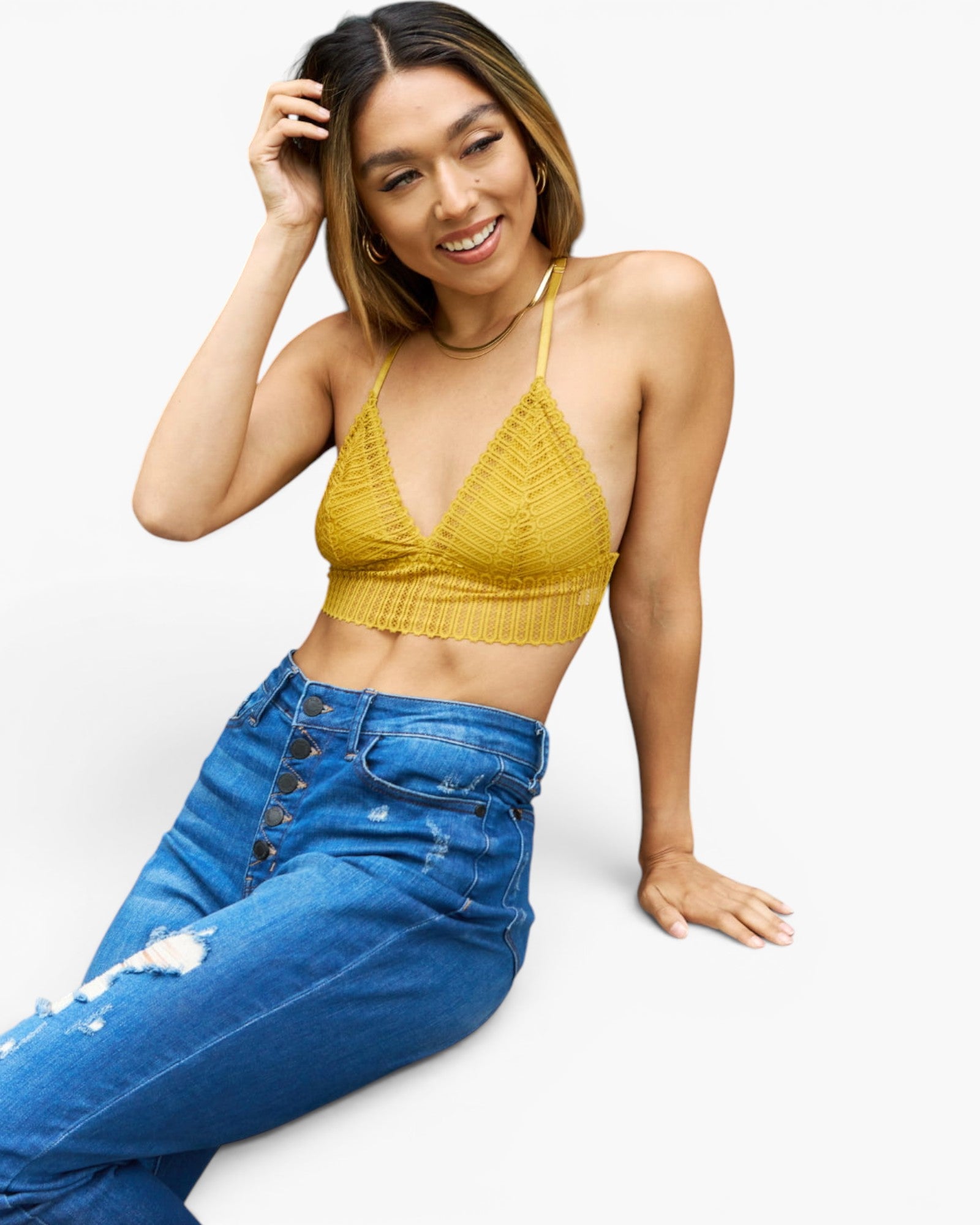 A woman wearing a textured mustard yellow triangle halter crop top and blue jeans, posing against a clean white background.