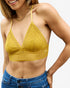 A woman wearing a yellow crochet triangle bralette top with thin straps and a scalloped underband, paired with blue jeans against a light gray studio background.