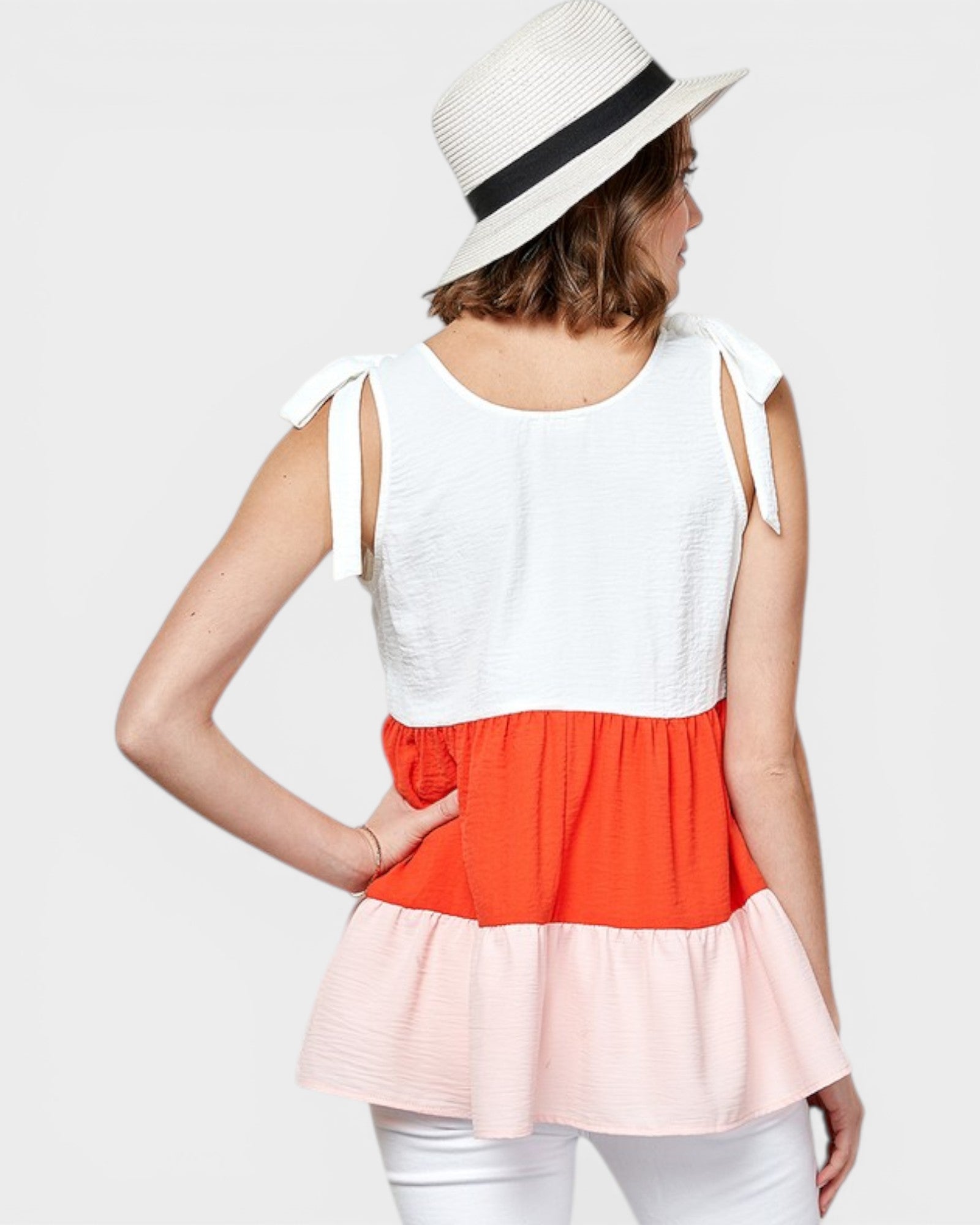 Woman wearing a white, orange, and pink top with a white hat on a light gray background