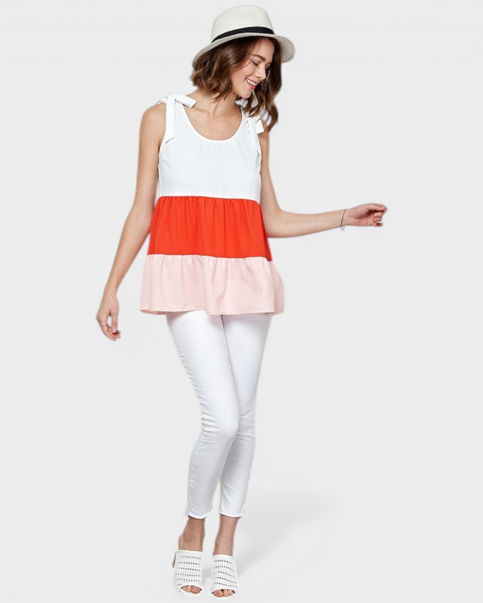 Woman wearing a colorful layered top and white pants on a plain background