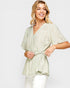 Woman wearing a light green floral wrap top on a white background