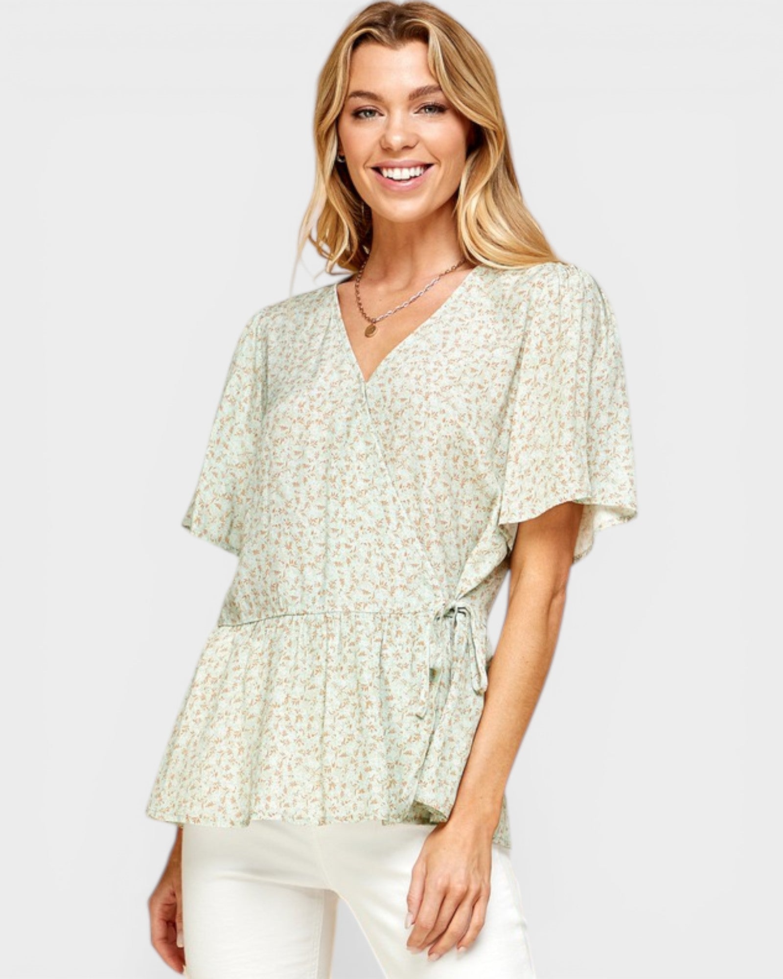 Woman wearing a light green floral blouse with white pants on a plain background