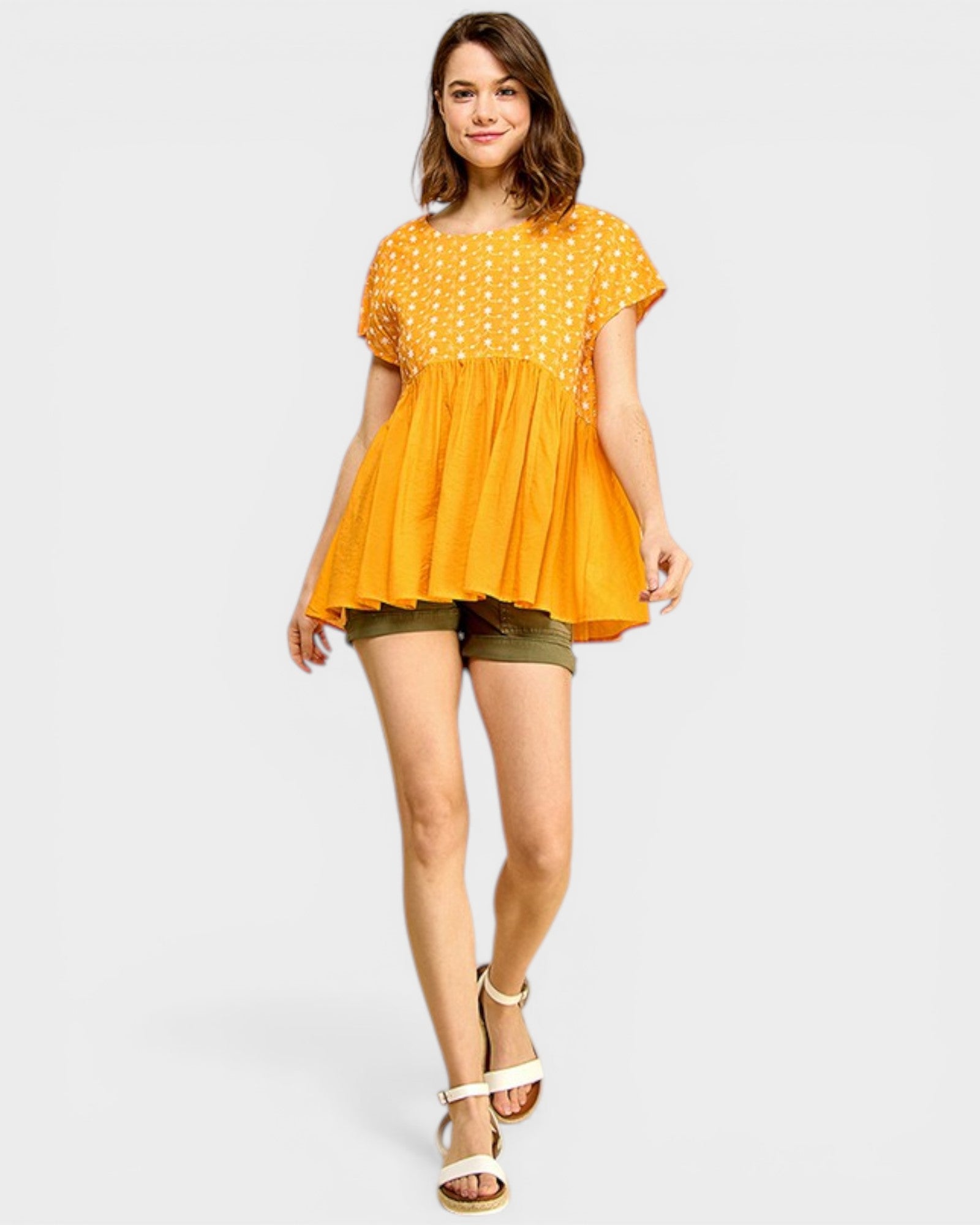 Woman wearing a yellow polka dot blouse and green shorts on a white background