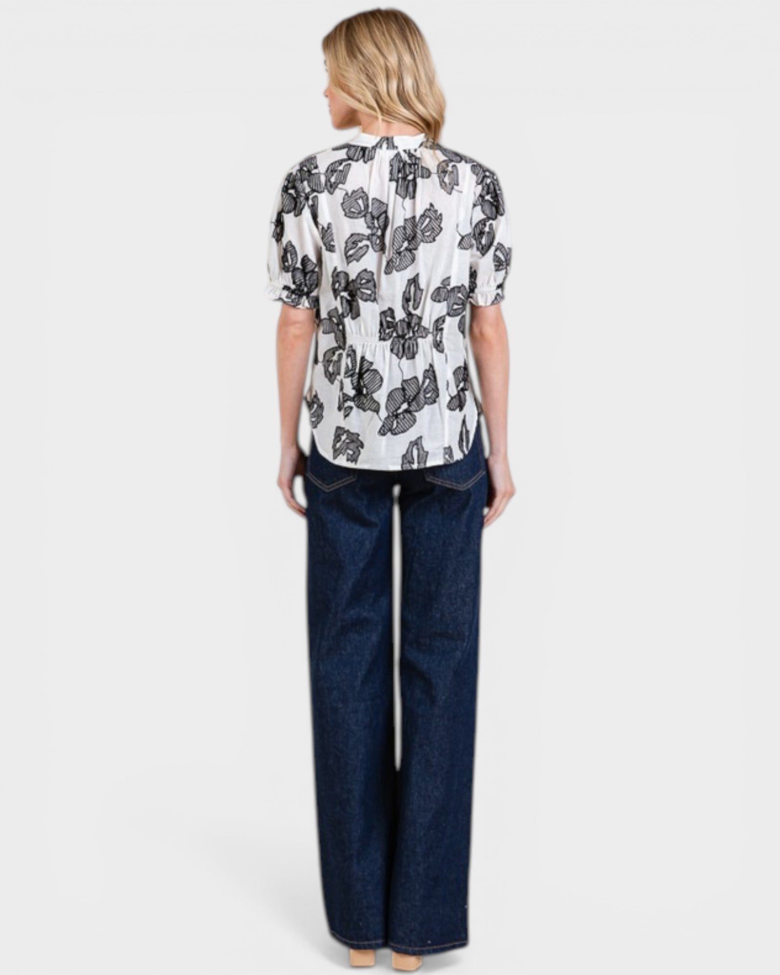 Woman wearing a patterned blouse and dark blue pants on a white background