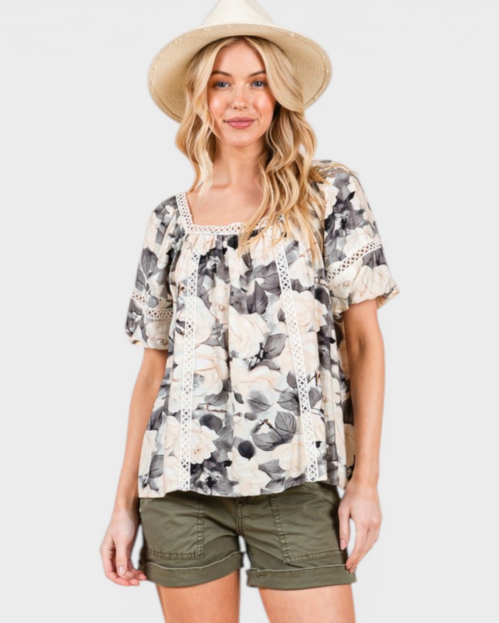 Woman wearing a floral blouse and green shorts with a beige hat on a light gray background