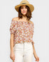 Woman wearing a floral off-shoulder top and straw hat on a light gray background