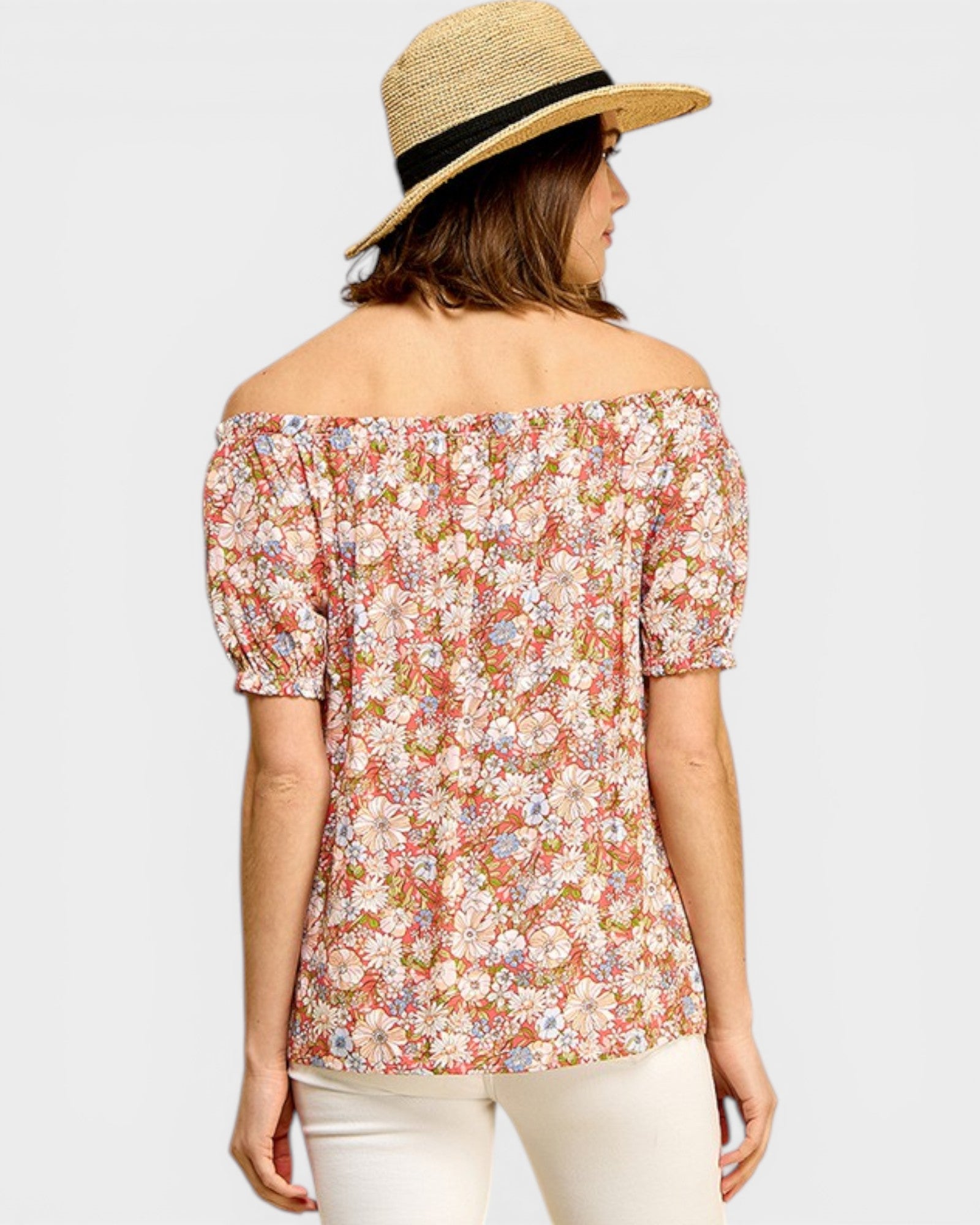 Woman wearing a floral off-shoulder top and straw hat on a light gray background