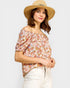 Woman wearing a floral off-shoulder top and straw hat on a plain background
