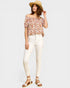 Woman wearing a floral off-shoulder top and white pants on a plain background