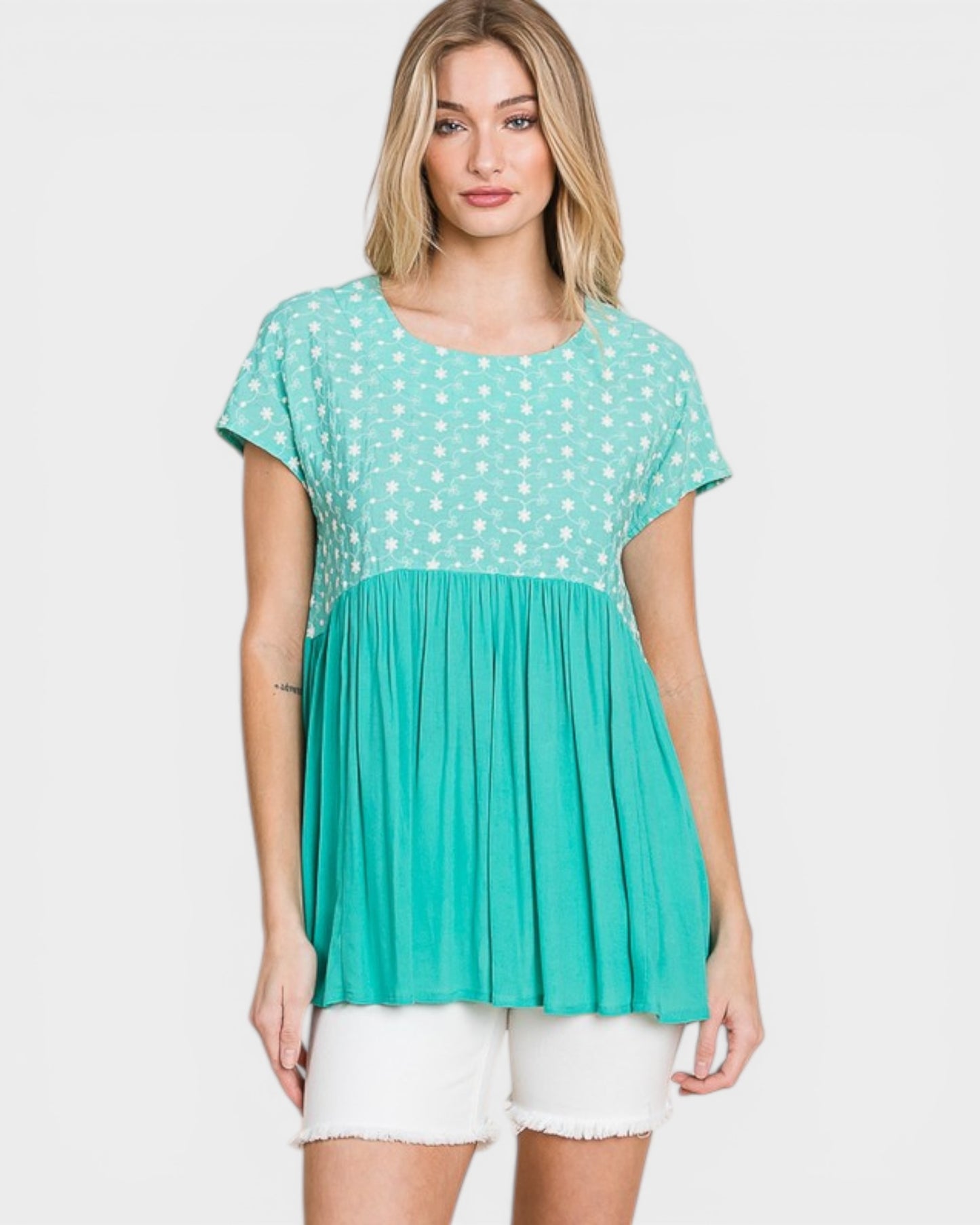 Woman wearing a green polka dot top and white shorts on a light gray background