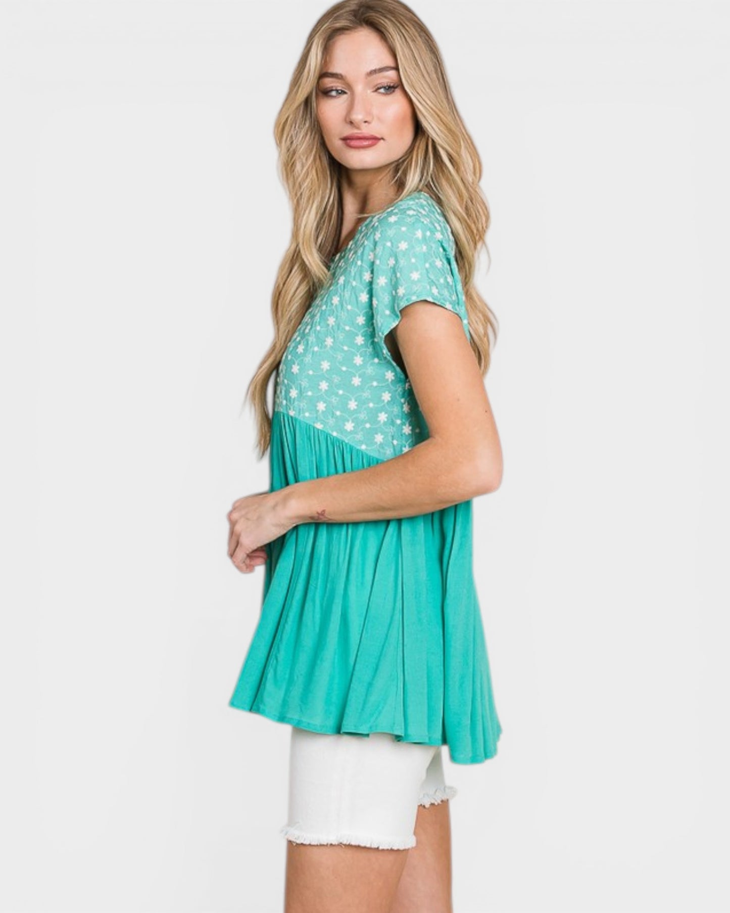 Woman wearing a teal and white polka dot top with a pleated skirt on a white background