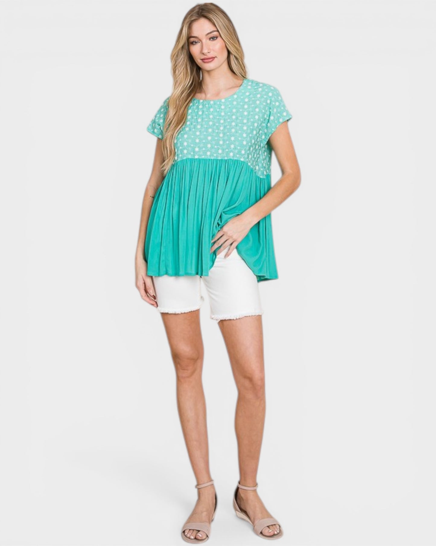 Woman wearing a teal and white polka dot top with white shorts on a white background