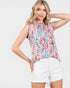 Woman wearing a colorful sleeveless top and white shorts on a plain background