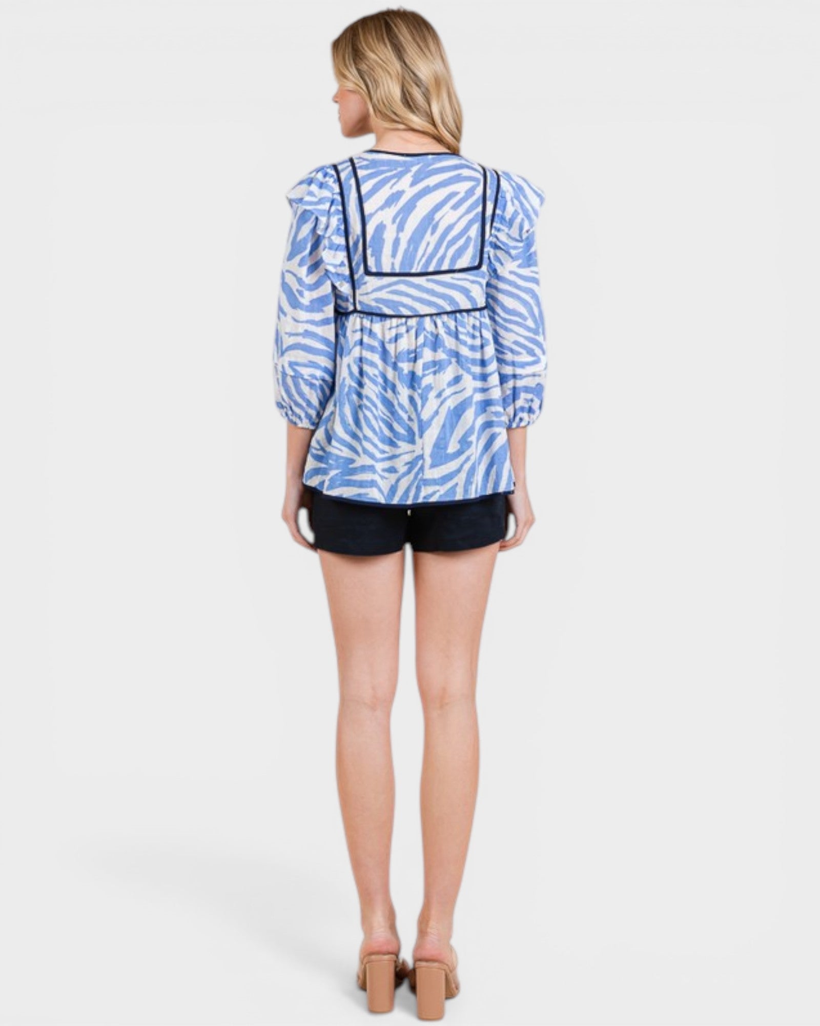 Woman wearing a blue and white patterned top with black shorts on a white background
