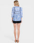 Woman wearing a blue and white patterned top with black shorts on a white background