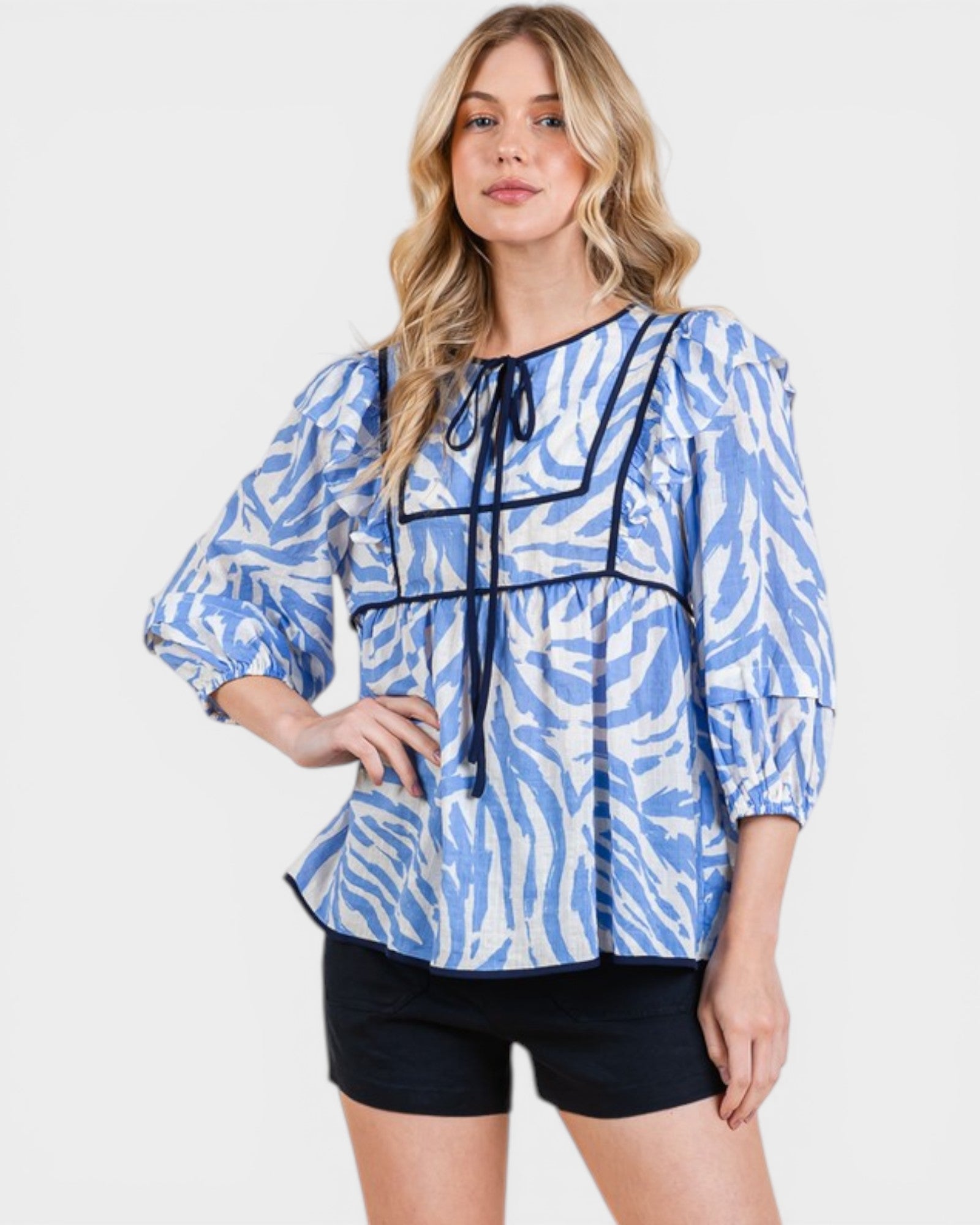 Woman wearing a blue and white patterned blouse with black trim on a white background