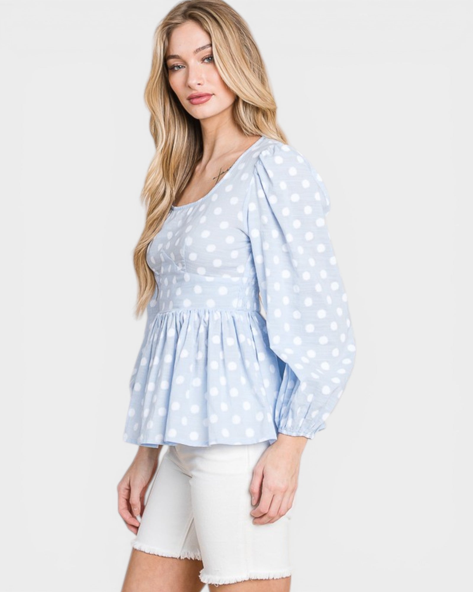Woman wearing a light blue polka dot blouse with white shorts on a white background