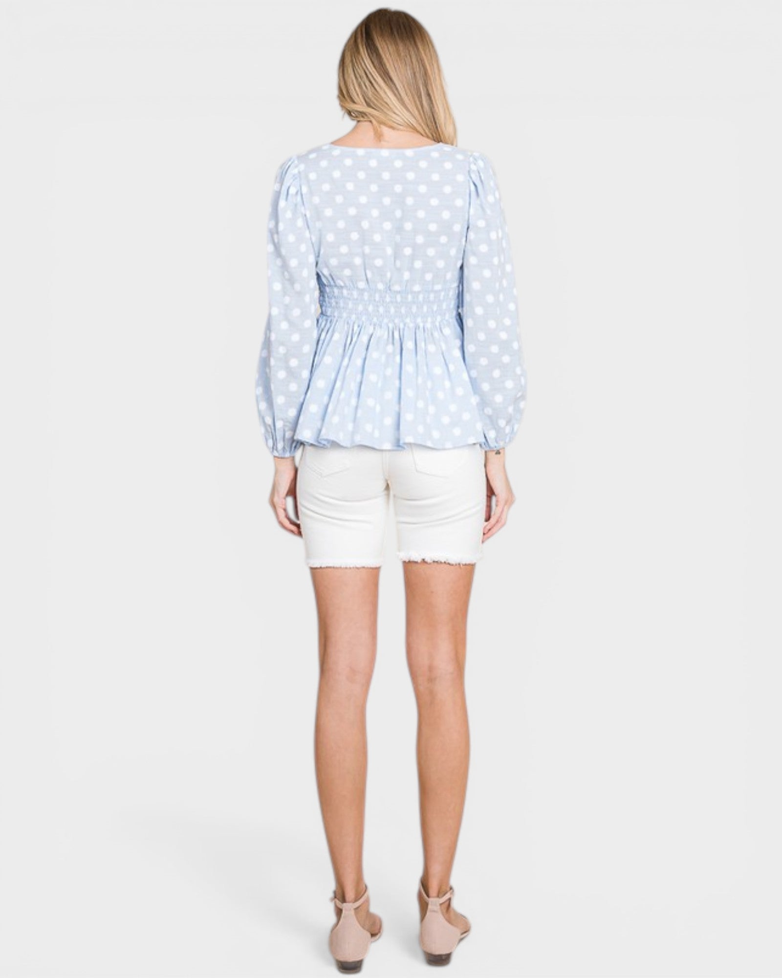 Woman wearing a light blue polka dot blouse and white shorts on a plain background