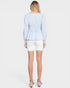 Woman wearing a light blue polka dot blouse and white shorts on a plain background