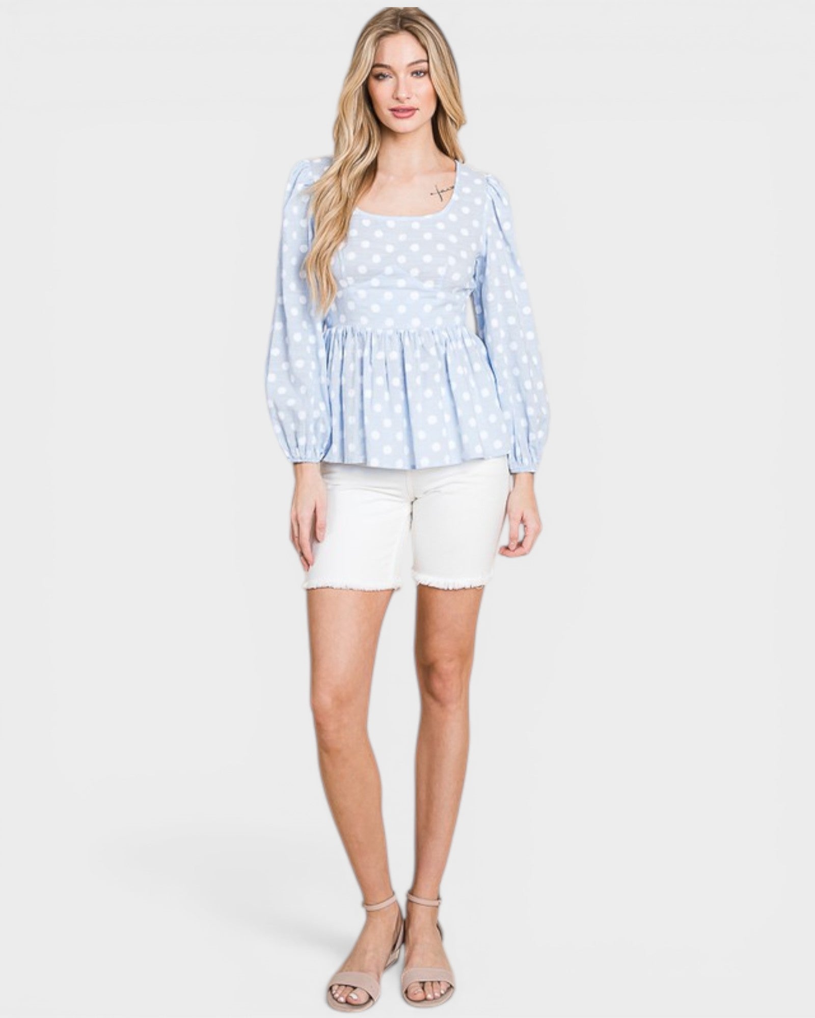 Woman wearing a light blue polka dot blouse and white shorts on a white background