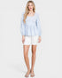 Woman wearing a light blue polka dot blouse and white shorts on a white background